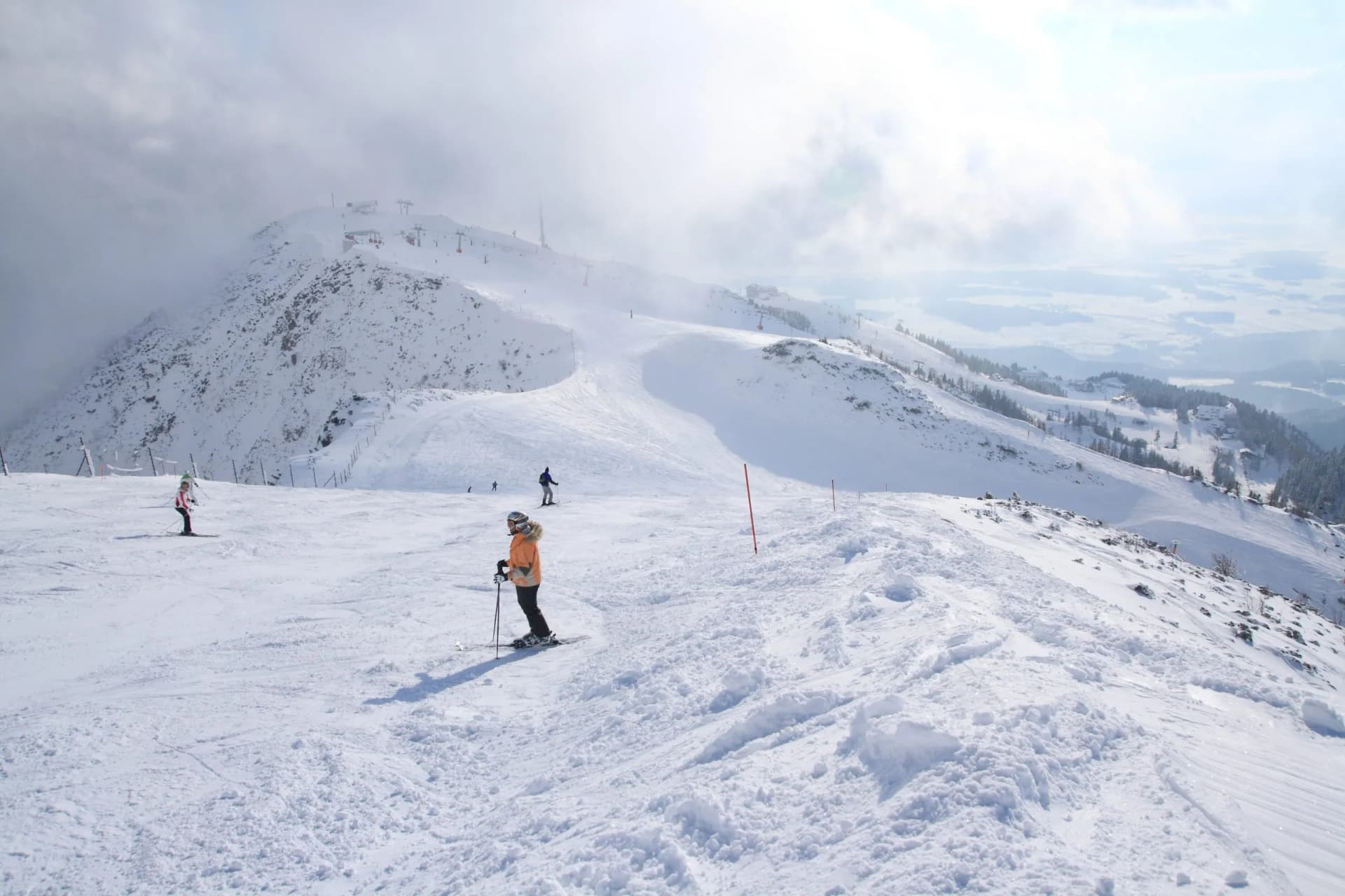 Skiers on a snowy slope at Krvavec mountain resort with fog and distant valley views.