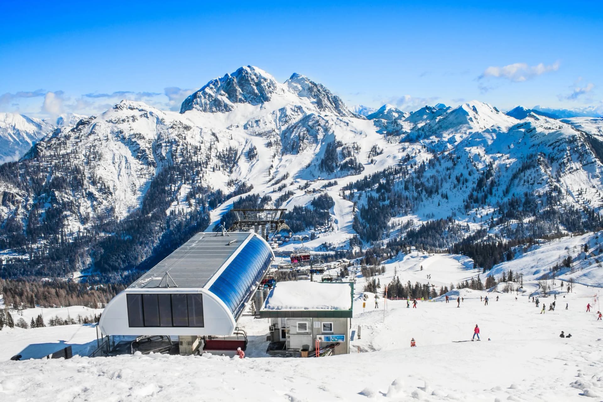 Skiers on snowy slope near gondola station with large snow-covered mountains in Nassfeld.