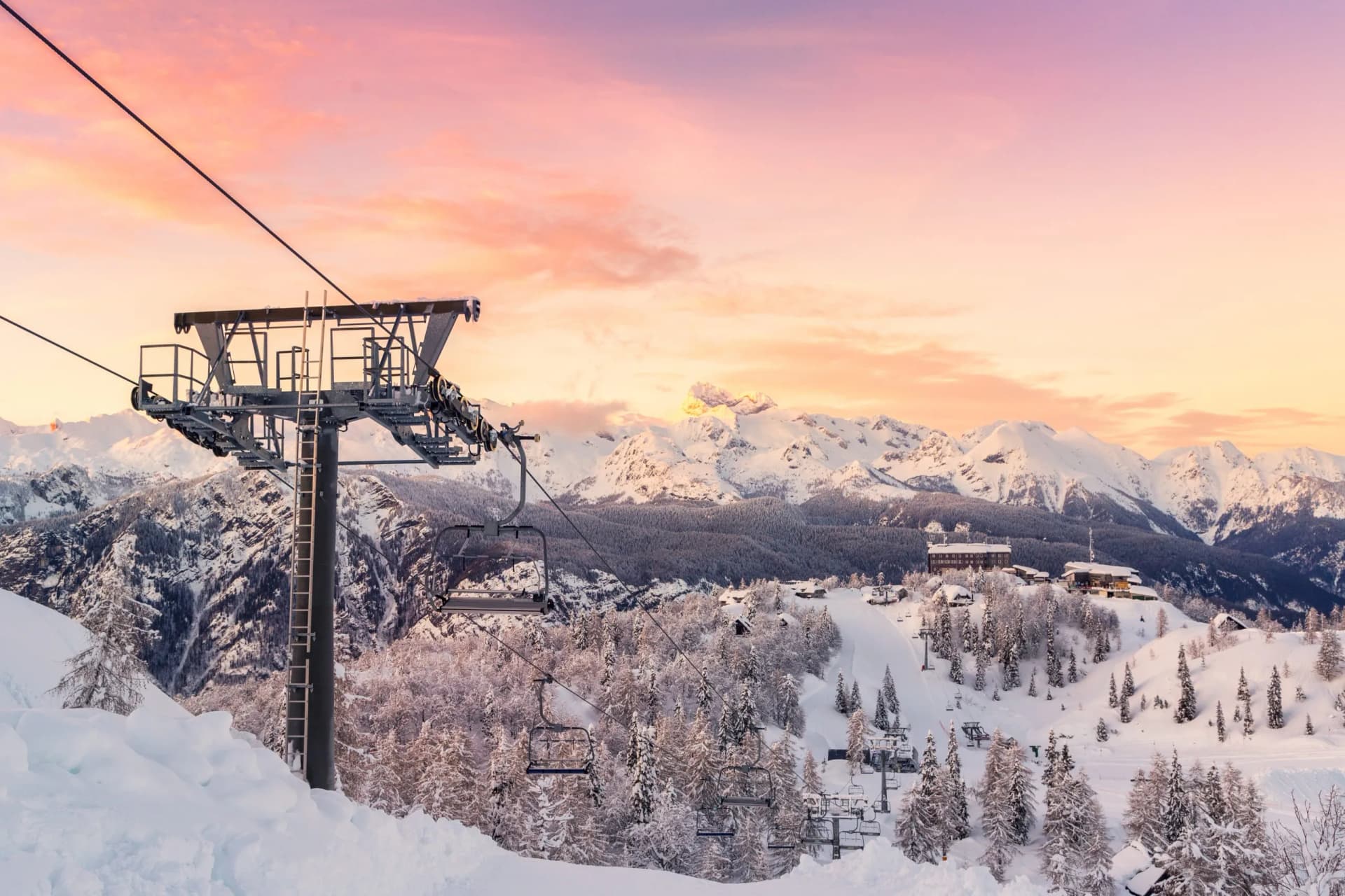 Ski lift tower and empty chairs over snowy mountain landscape at sunset