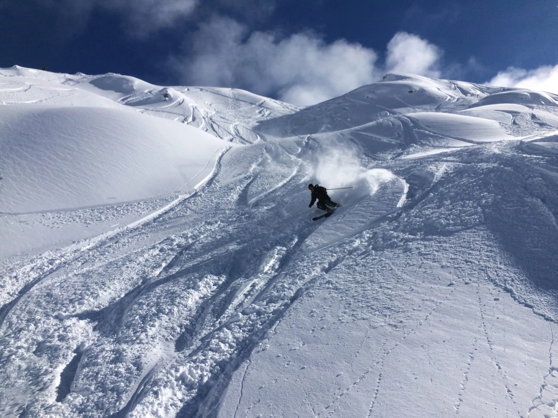 Skier making powder turns down steep, snow-covered mountain slope under blue sky