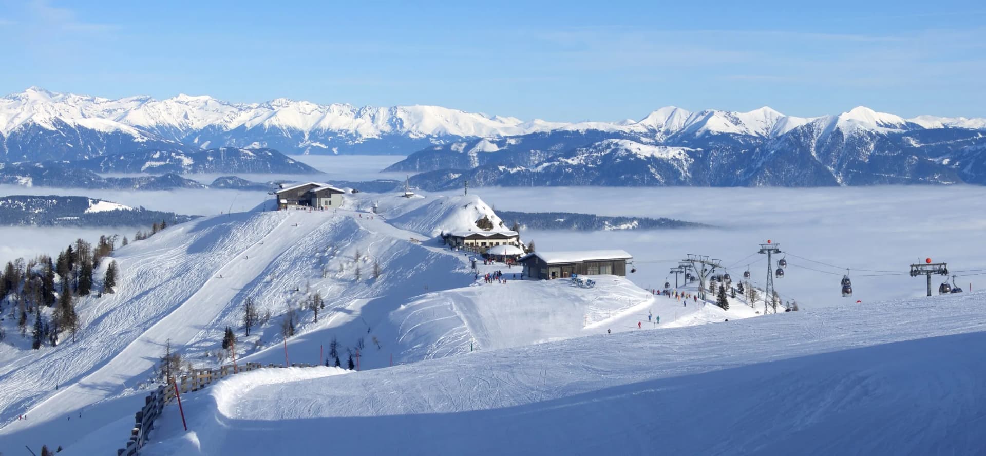 Ski resort panorama with snow-covered slopes, mountain lodges, and gondola lift above fog.