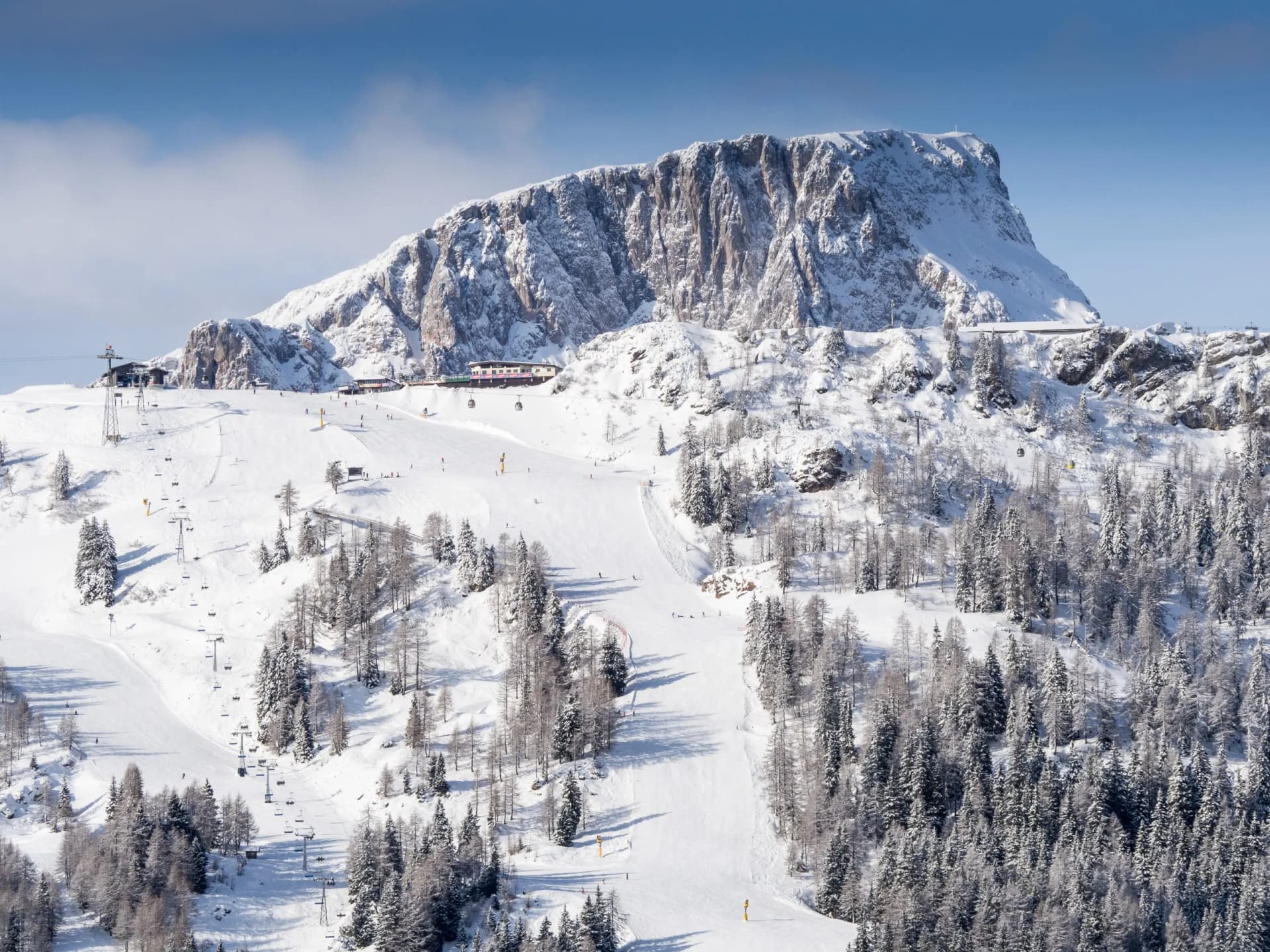 Ski slopes at Nassfeld with snow-covered mountains, chairlifts, and skiers under a blue sky.