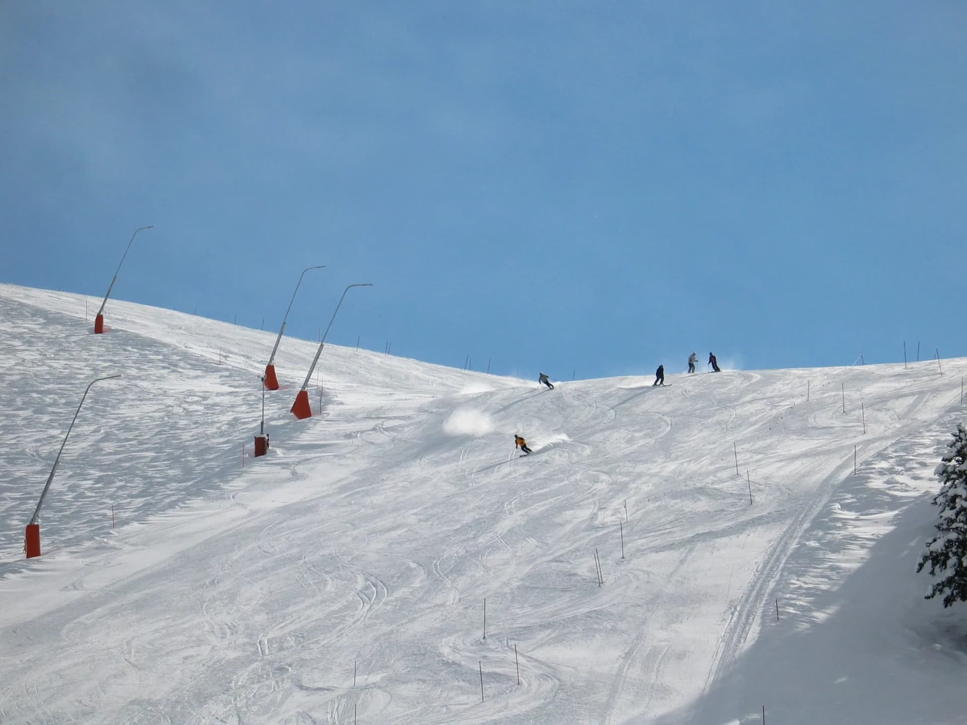 Skiers descending a snowy slope under a clear blue sky at Krvavec ski resort.