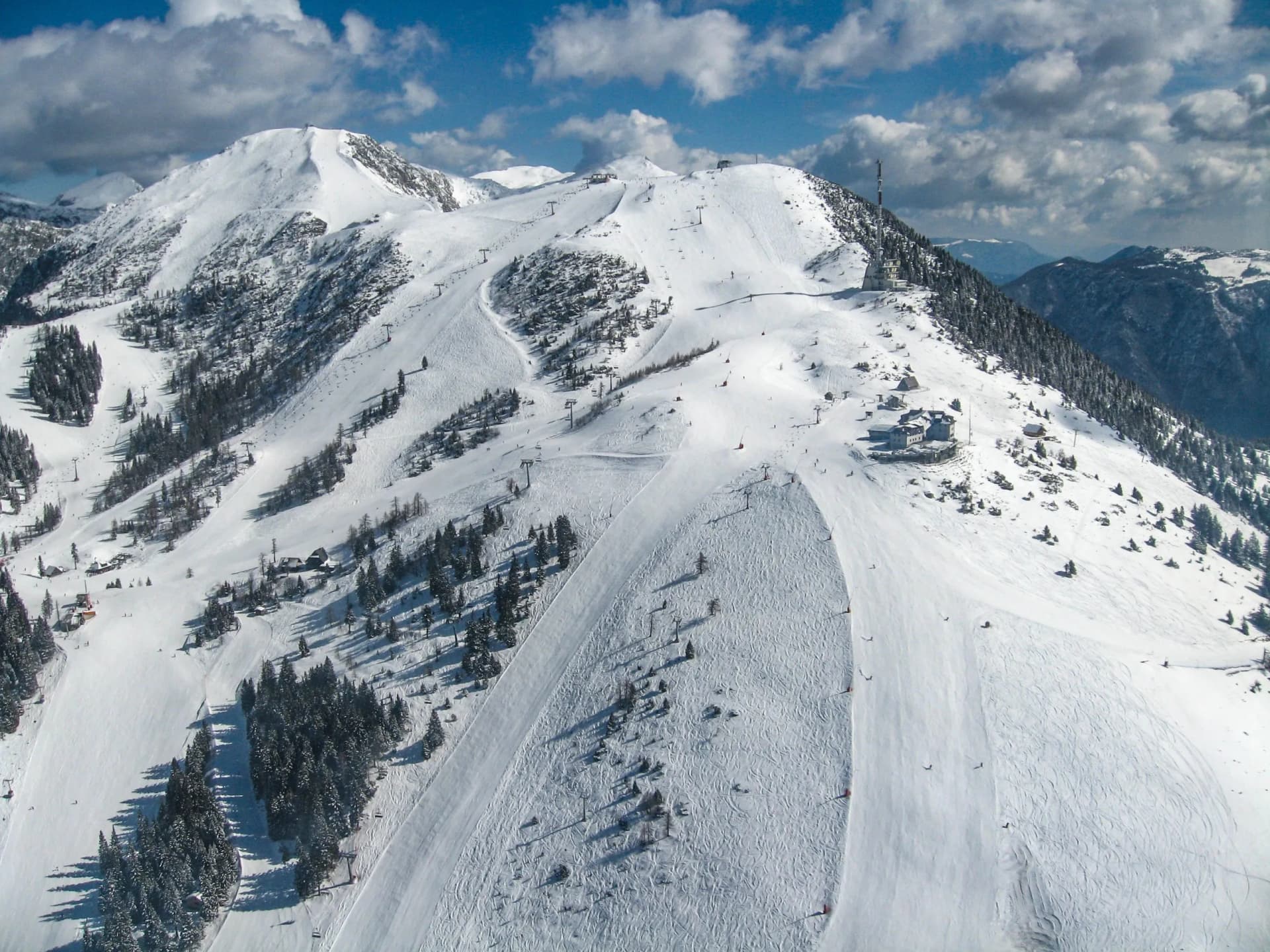 Bird's-eye view of Krvavec ski slopes covered in snow with chairlifts and scattered pine trees.