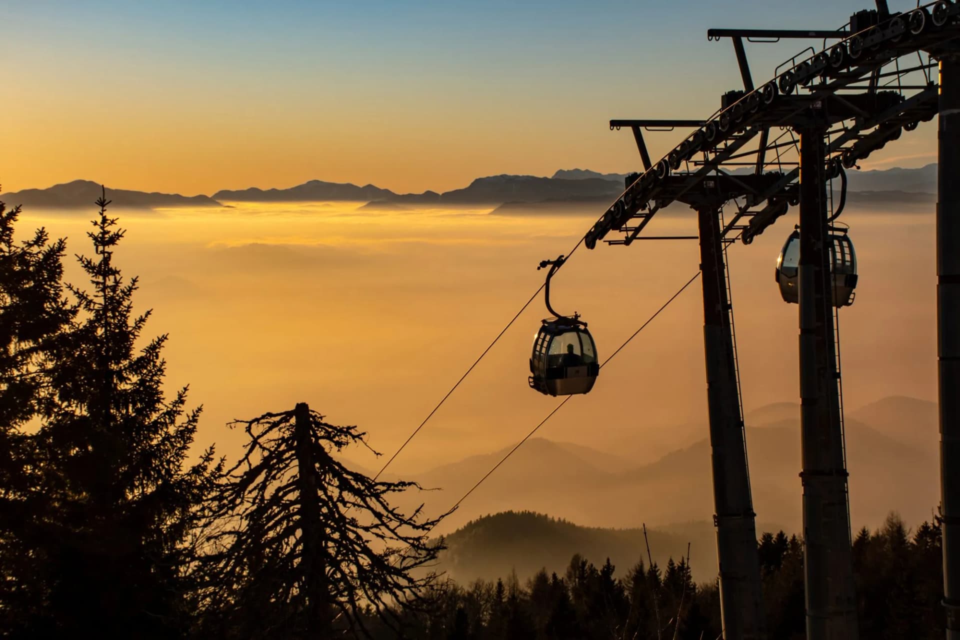 Cable car gondolas above fog-filled valley and mountain silhouettes at sunset