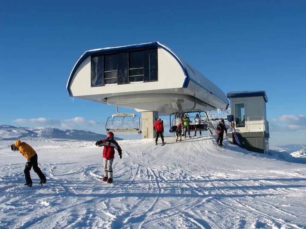 Skiers and snowboarders near the Krvavec ski lift station on a sunny, snowy mountain slope.