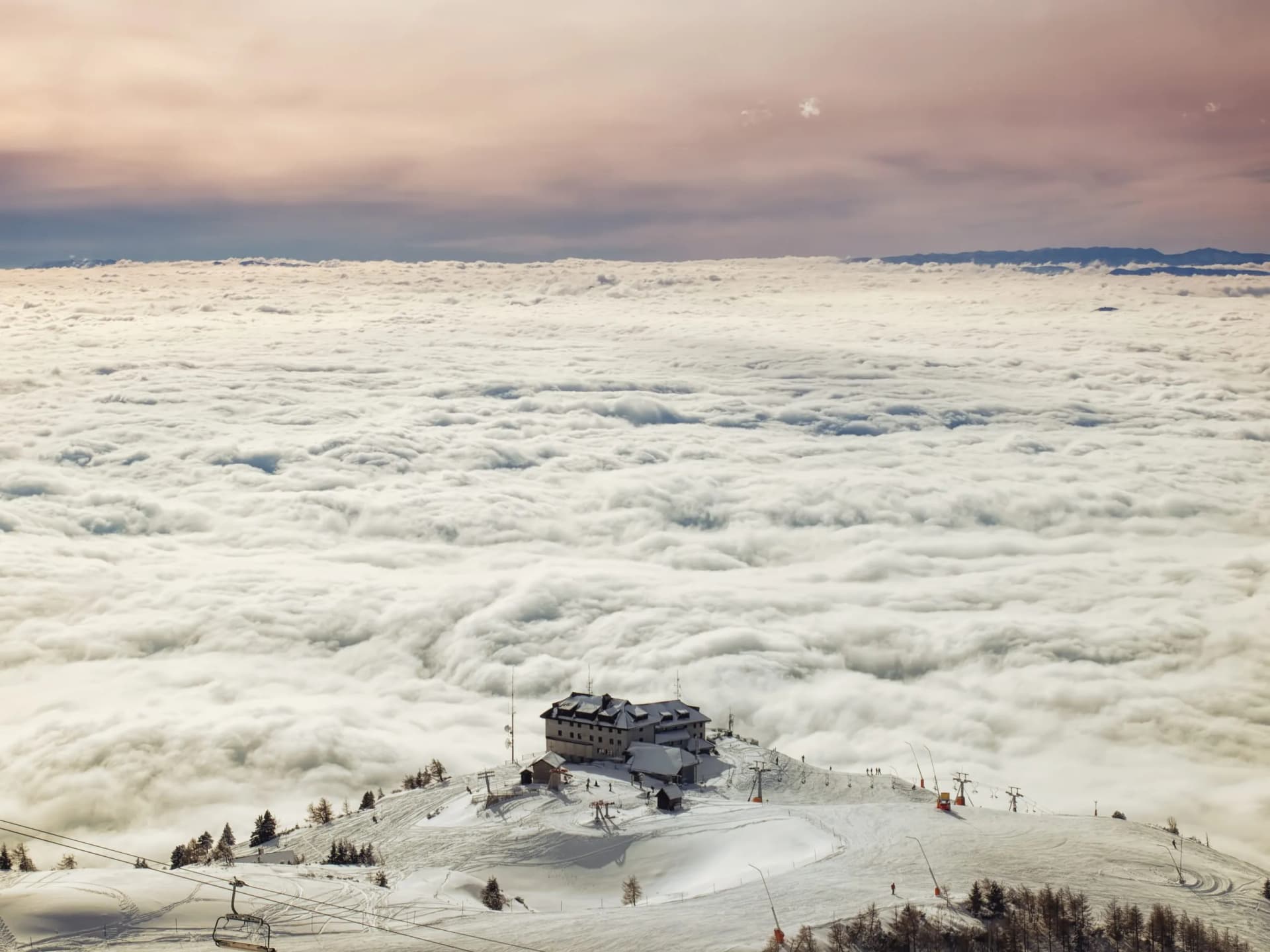 Ski resort building above sea of clouds at Krvavec with chairlifts and snow-covered slopes.