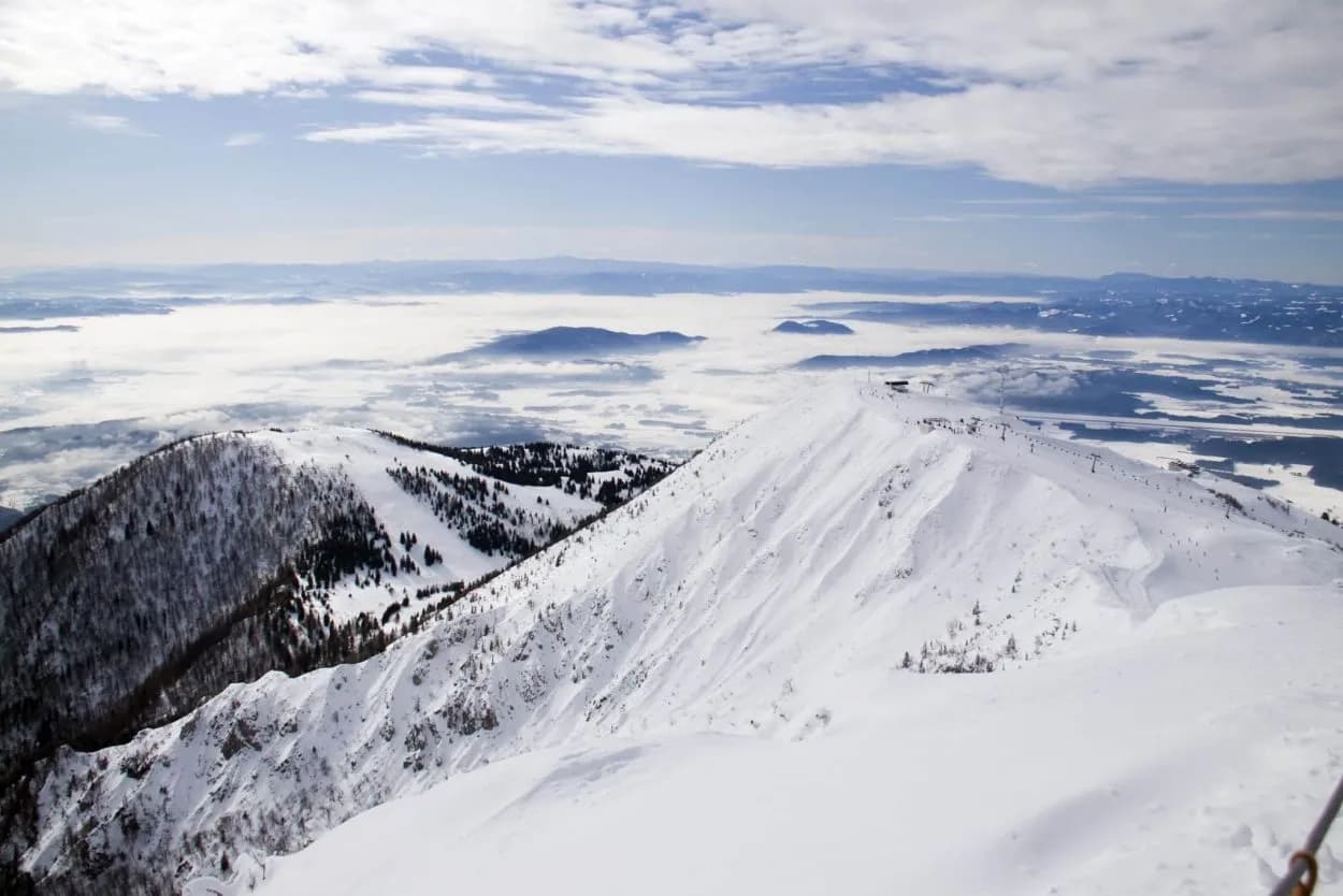 Snowy mountain ridge at Krvavec ski resort above low-lying clouds and distant peaks.