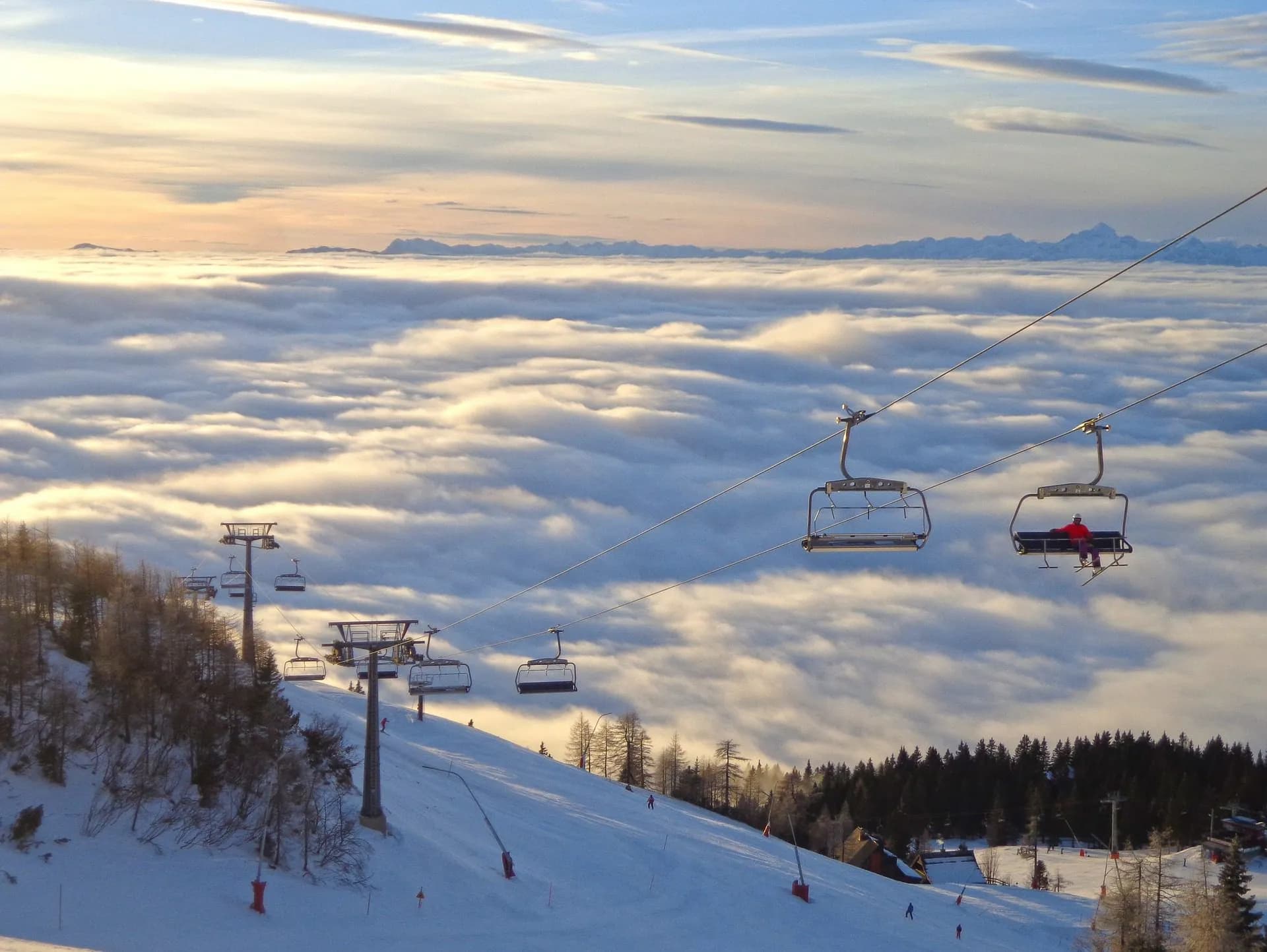 Ski lift chairs ascending snowy slope above sea of clouds with distant mountains at Krvavec.