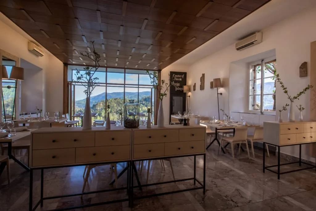 Restaurant dining room with light wood furniture and large windows overlooking green mountains near Bled.
