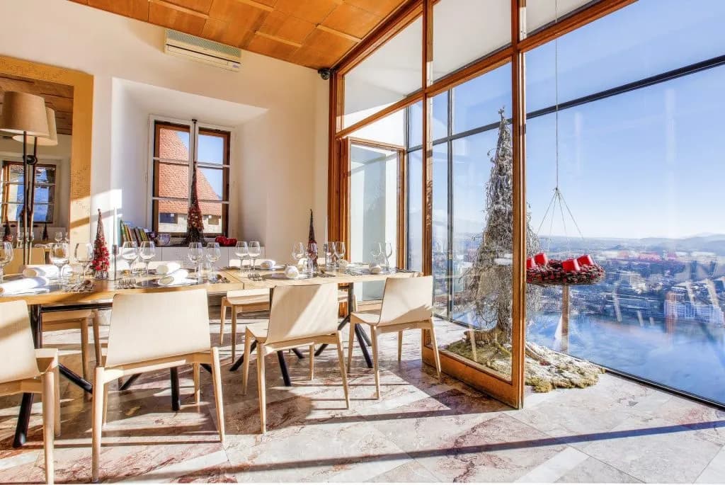 Dining room with set table and large windows overlooking a sunny city and water view.