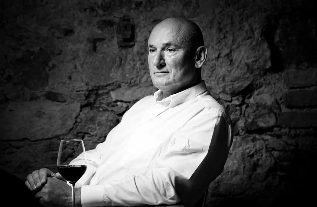 Man in white shirt holding a glass of red wine in a dimly lit cellar with stone walls in Ljubljana.