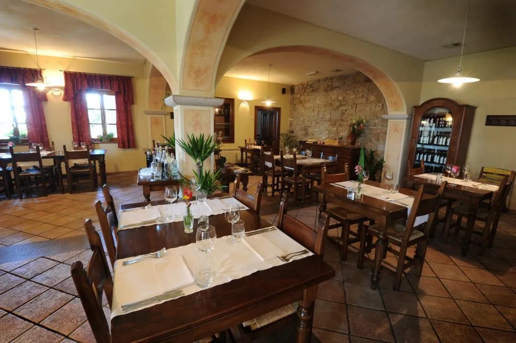 Dining room interior of Belica Restaurant in Goriška Brda with wooden tables and stone wall.
