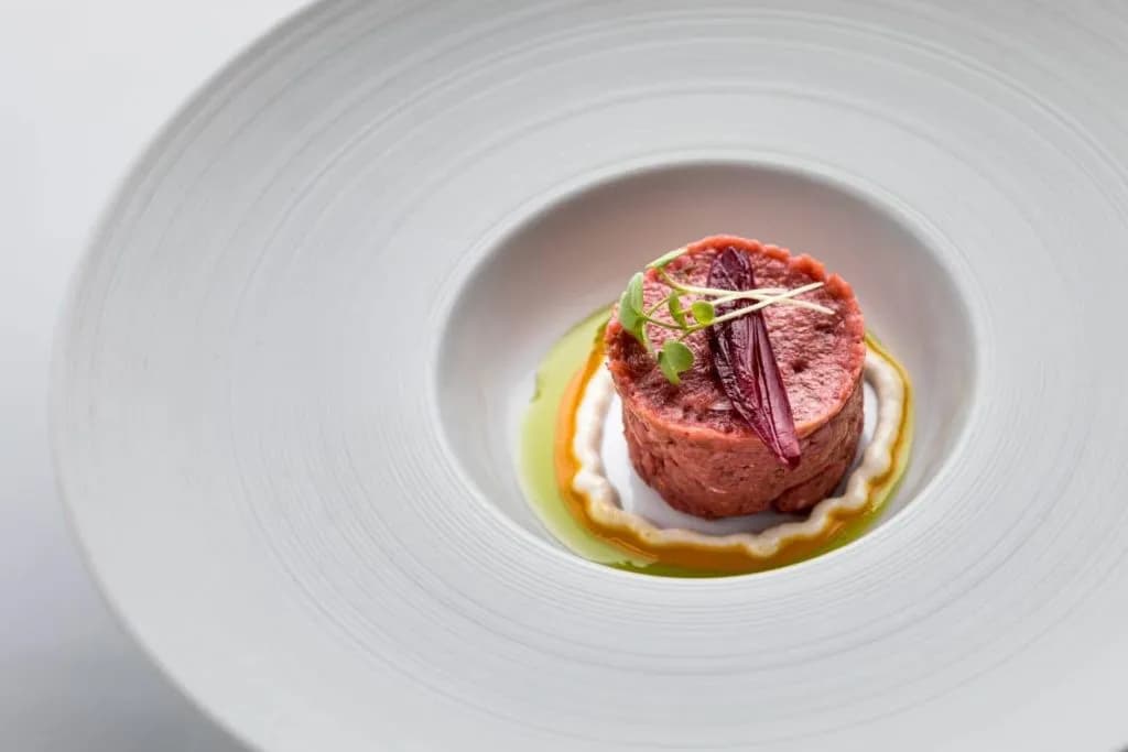 Steak tartare portioned and garnished on a wide white plate with sauce swirls