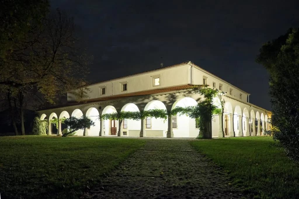 White building with arched colonnade illuminated at night, viewed from grassy lawn