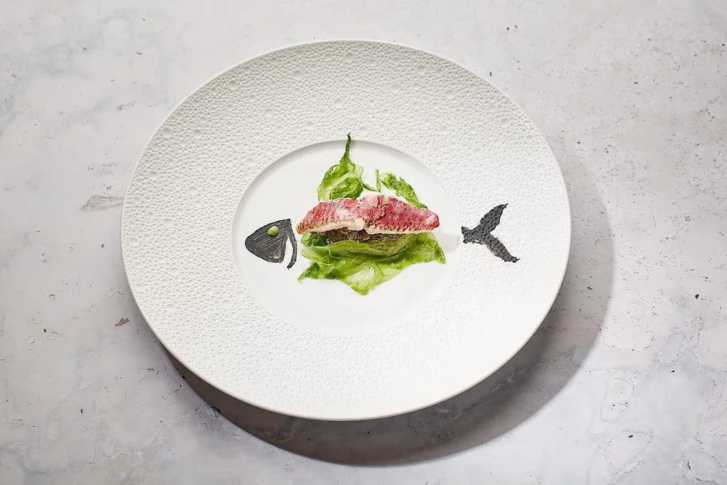Gourmet fish portion served on lettuce, creatively plated as a fish skeleton on a white dish.