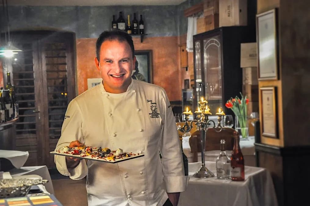 Chef Jure Tomic holding a plate of desserts in a warmly lit restaurant setting