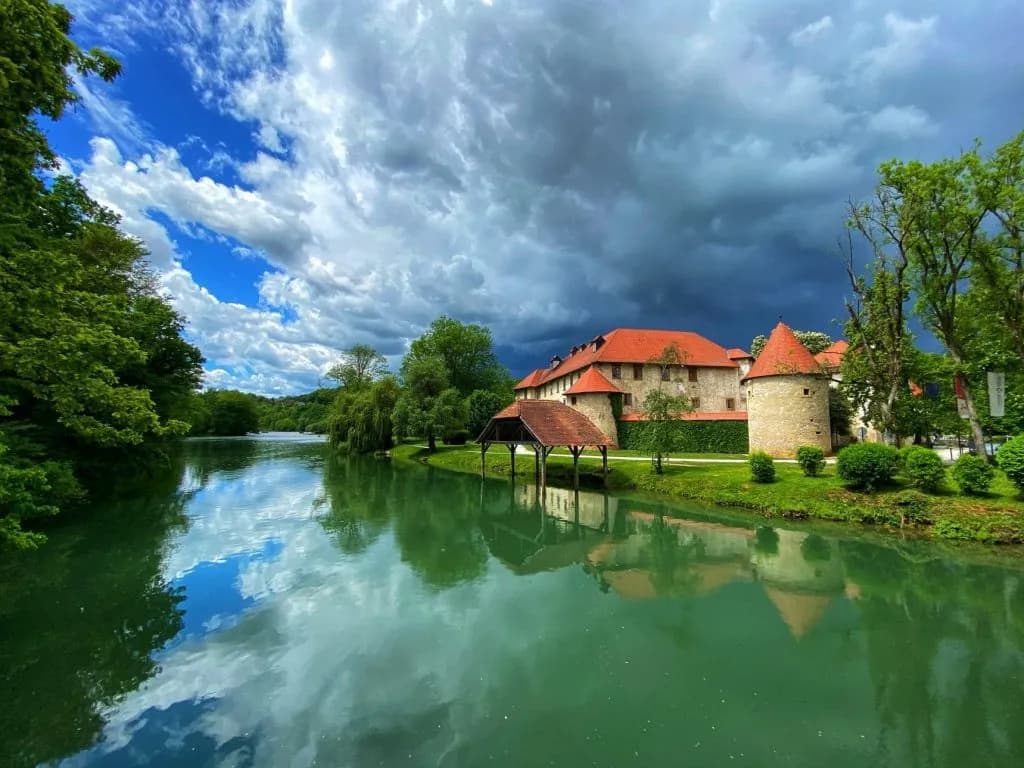 Otočec Castle in Dolenjska Region beside green river under dramatic cloudy sky