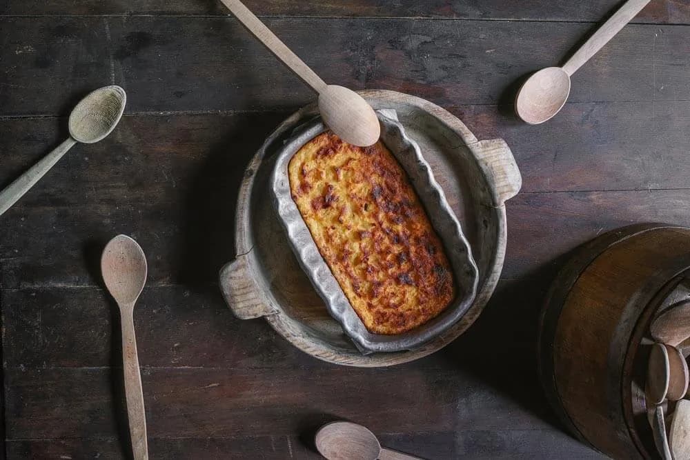 Baked polenta dish in a metal pan on a rustic wooden surface with wooden spoons.