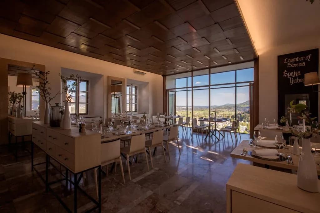 Restaurant dining room with modern tables and large windows overlooking a green valley near Bled.