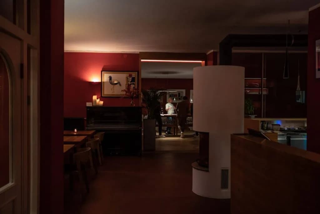 Dimly lit restaurant interior with red walls, a piano, and a white cylindrical fireplace.