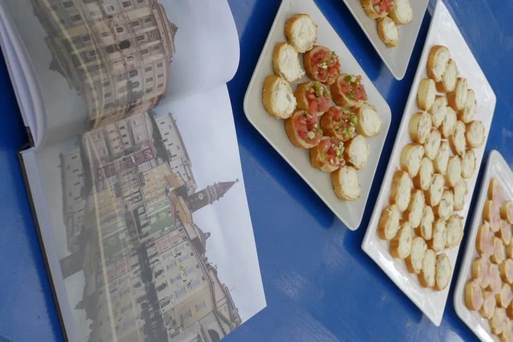 Open book showing colorful European buildings next to plates of bruschetta and bread canapés.
