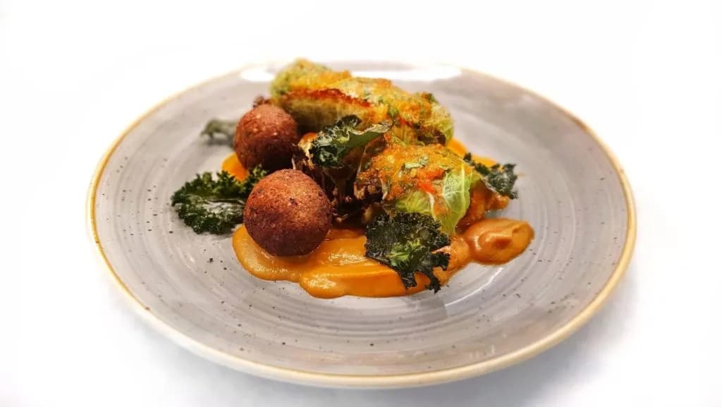 Stuffed cabbage rolls and croquettes on orange puree with kale, photographed by Enrico Piras.