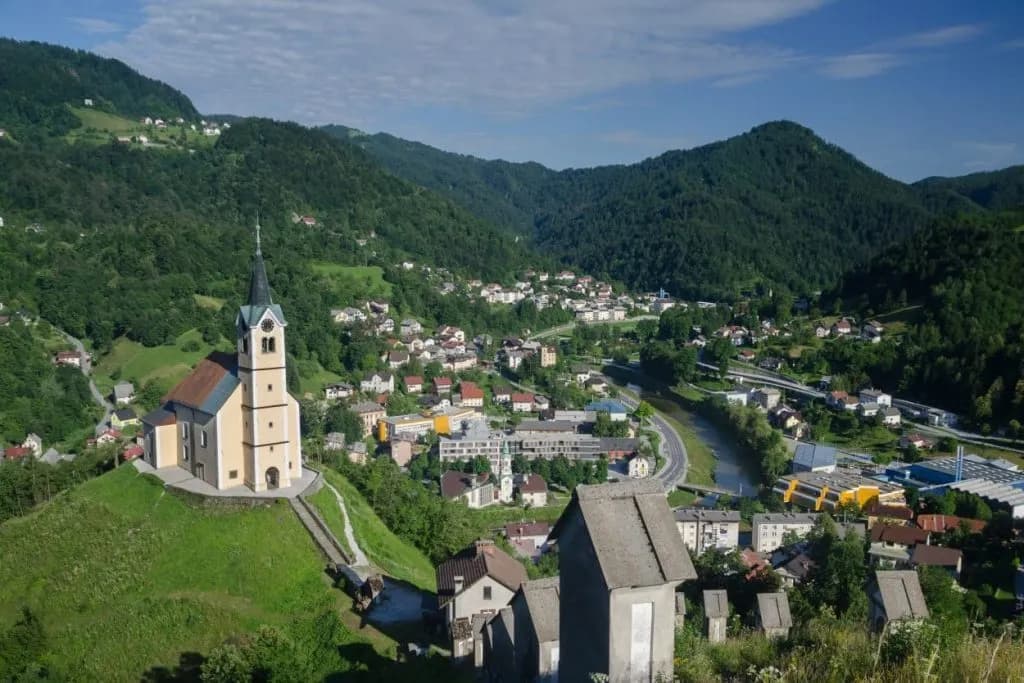 Church on a hill overlooking the town of Idrija nestled in green mountains.
