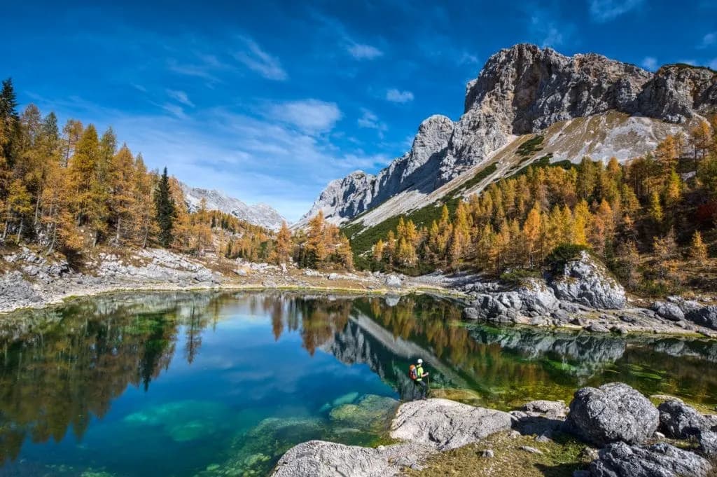 Triglav Lakes hiker by turquoise alpine lake with autumn foliage and rocky mountains.