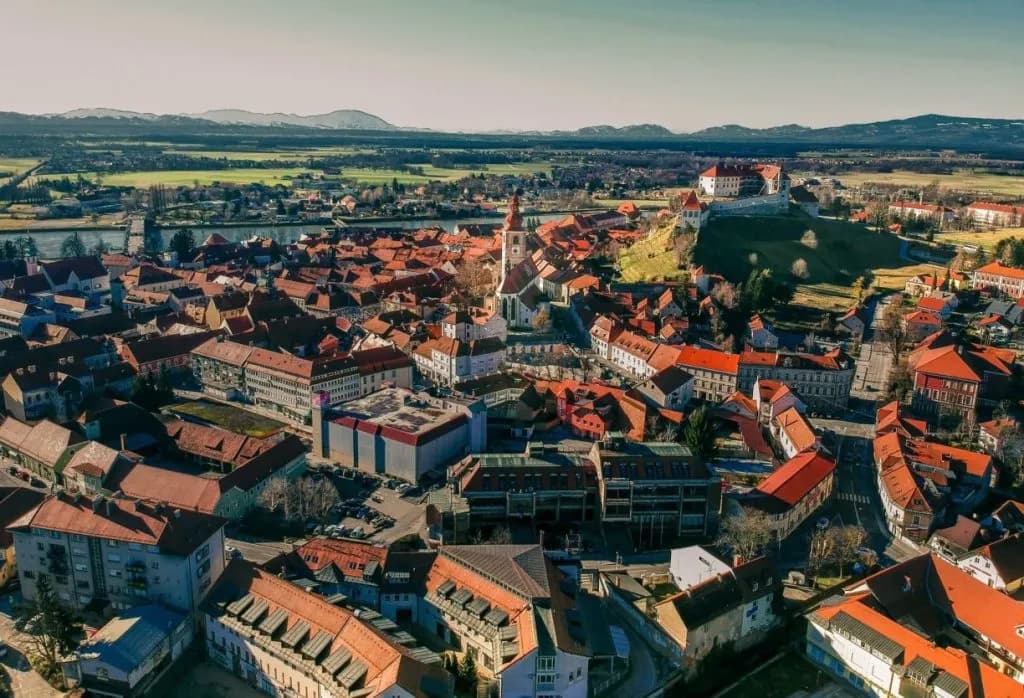 Aerial view of Ptuj Old Town with red roofs, a church tower, and a castle on a hill.