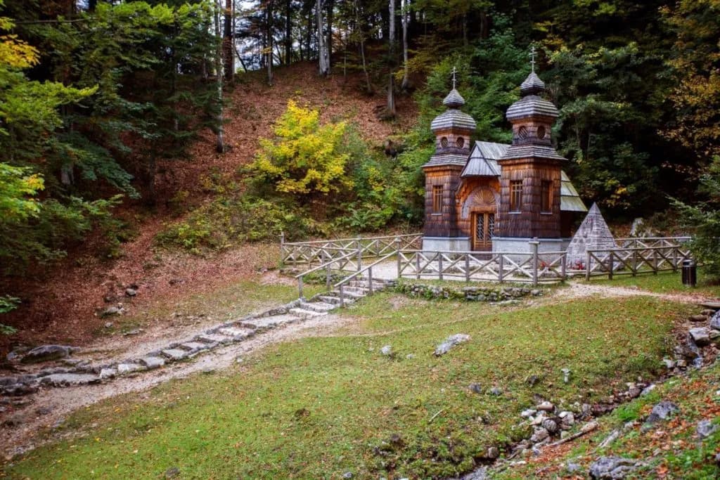 Wooden Russian chapel on Vogel surrounded by autumn forest and green meadow.