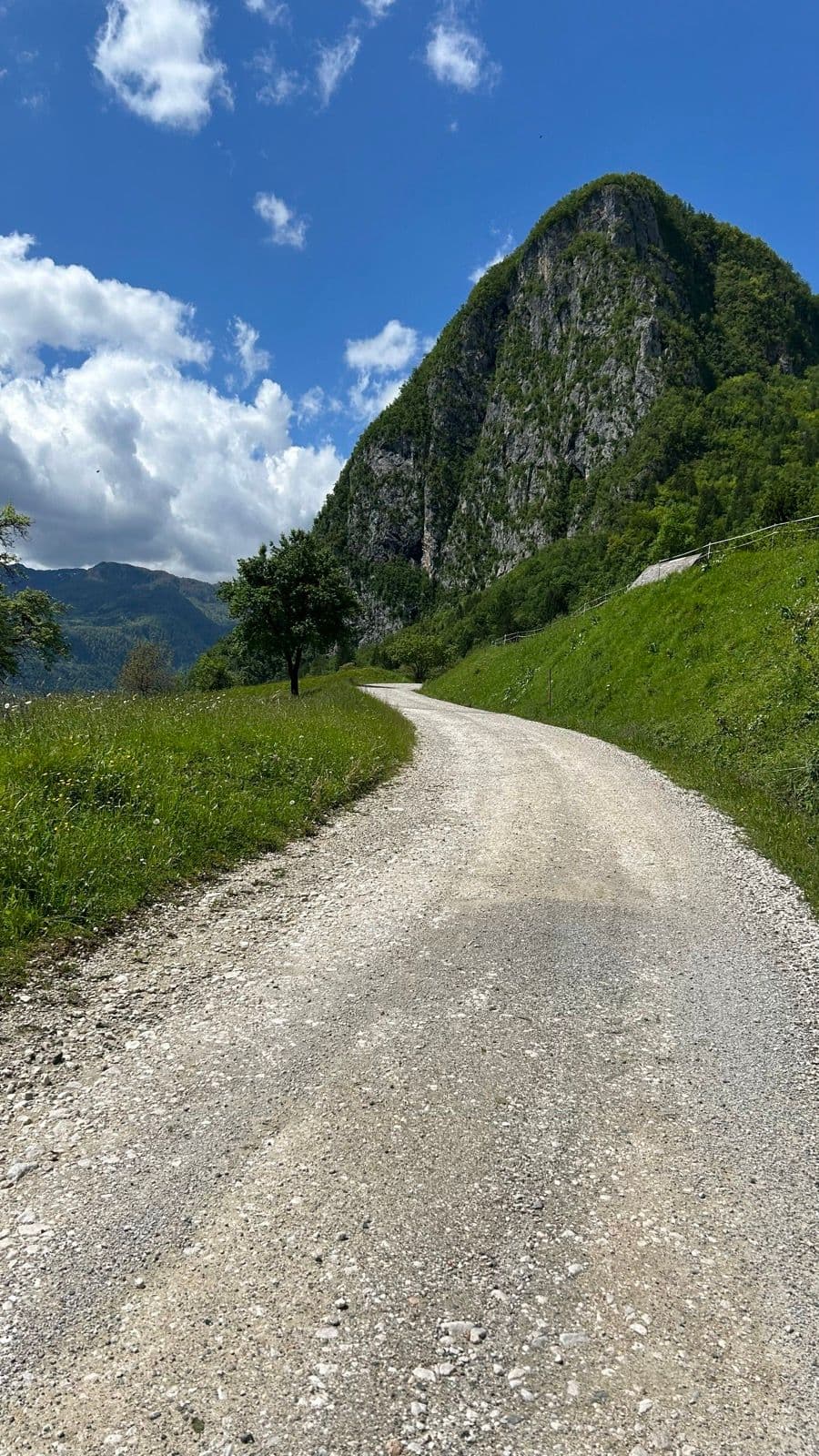 Gravel trail winding through a green mountain landscape under a blue sky with clouds.