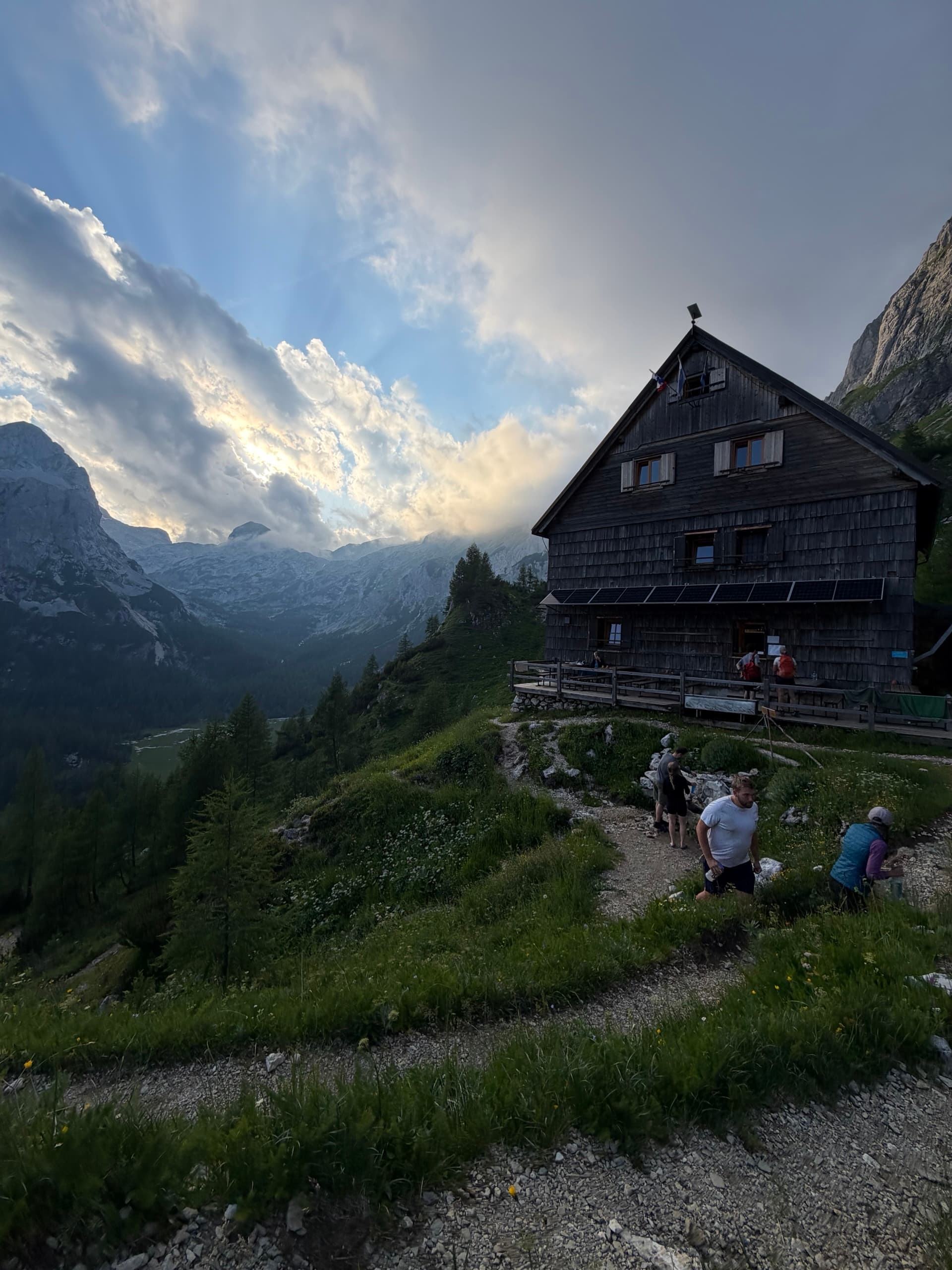 Wooden alpine mountain hut with hikers on trail during sunset rays