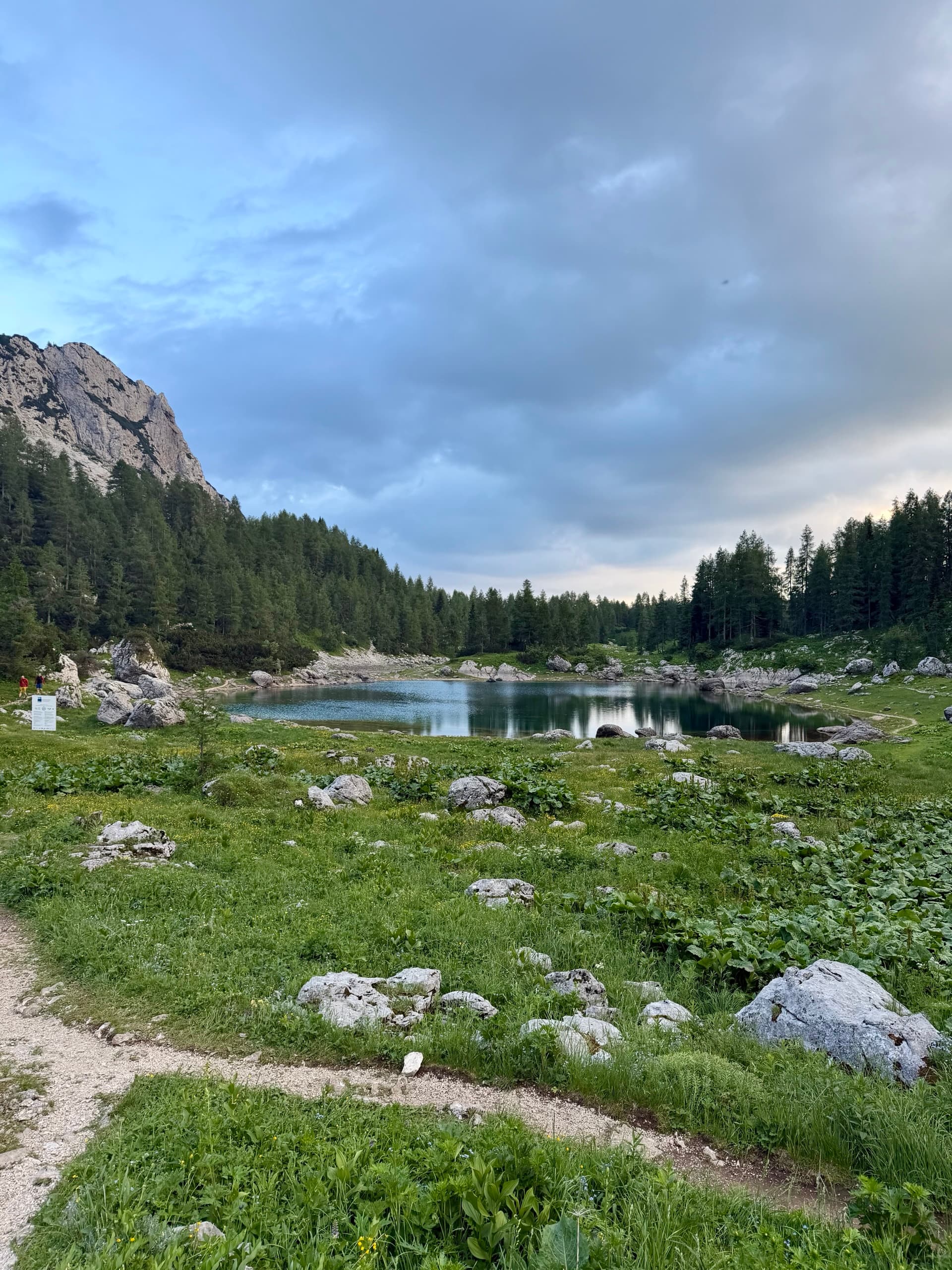 Alpine lake in Seven Lakes Valley surrounded by mountains, forest, and rocky meadow under a cloudy sky