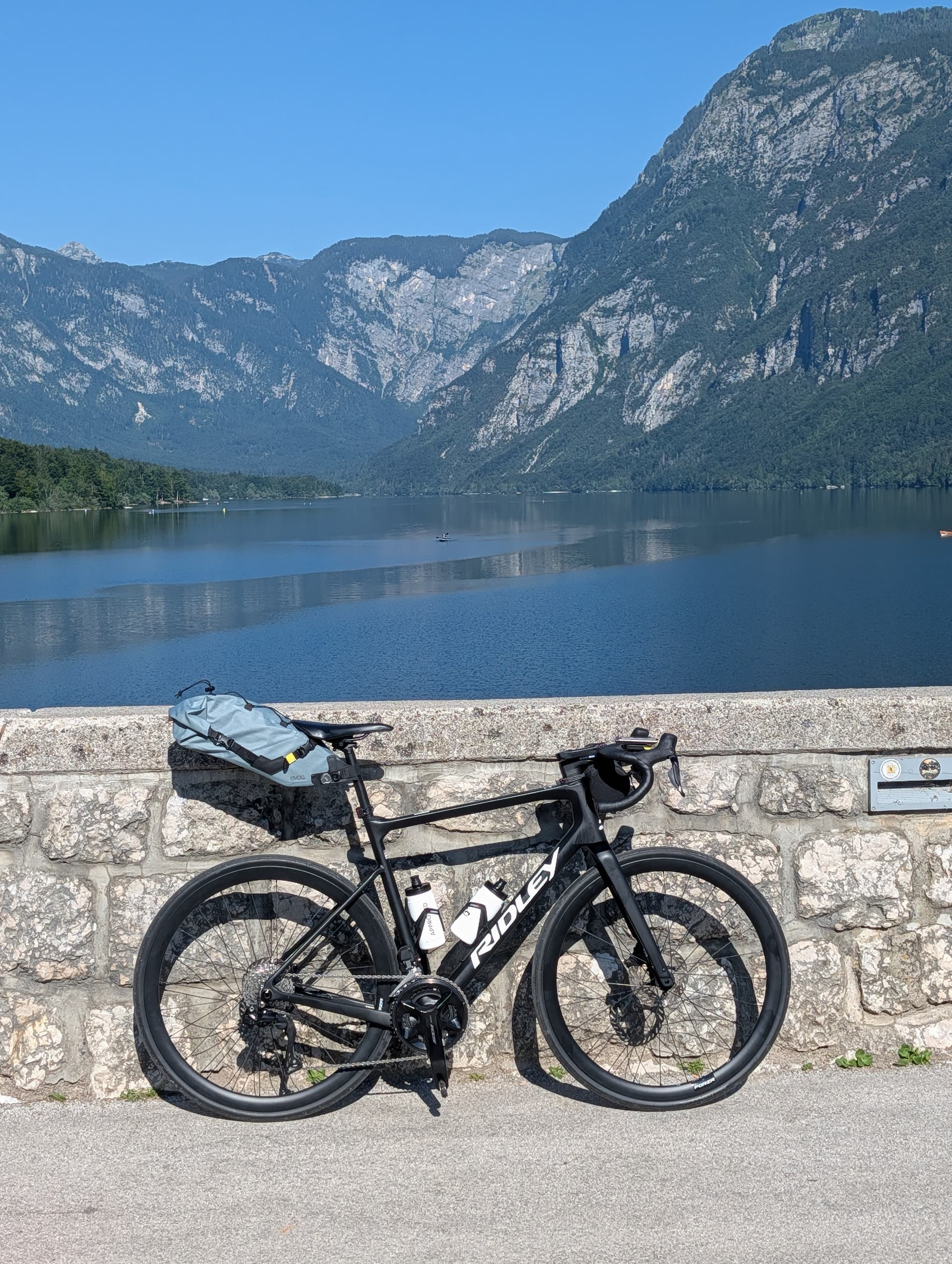 Black road bike parked against a stone wall at Lake Bohinj with mountain background