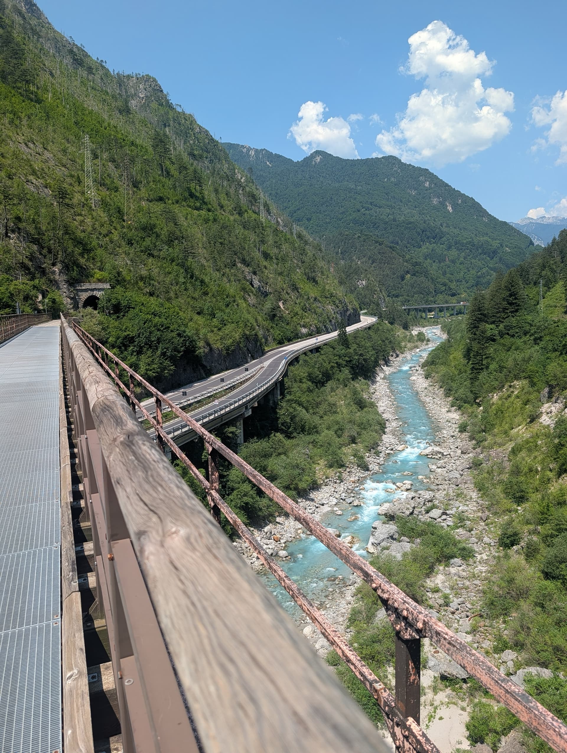 Metal cycle bridge beside turquoise river running through mountain valley