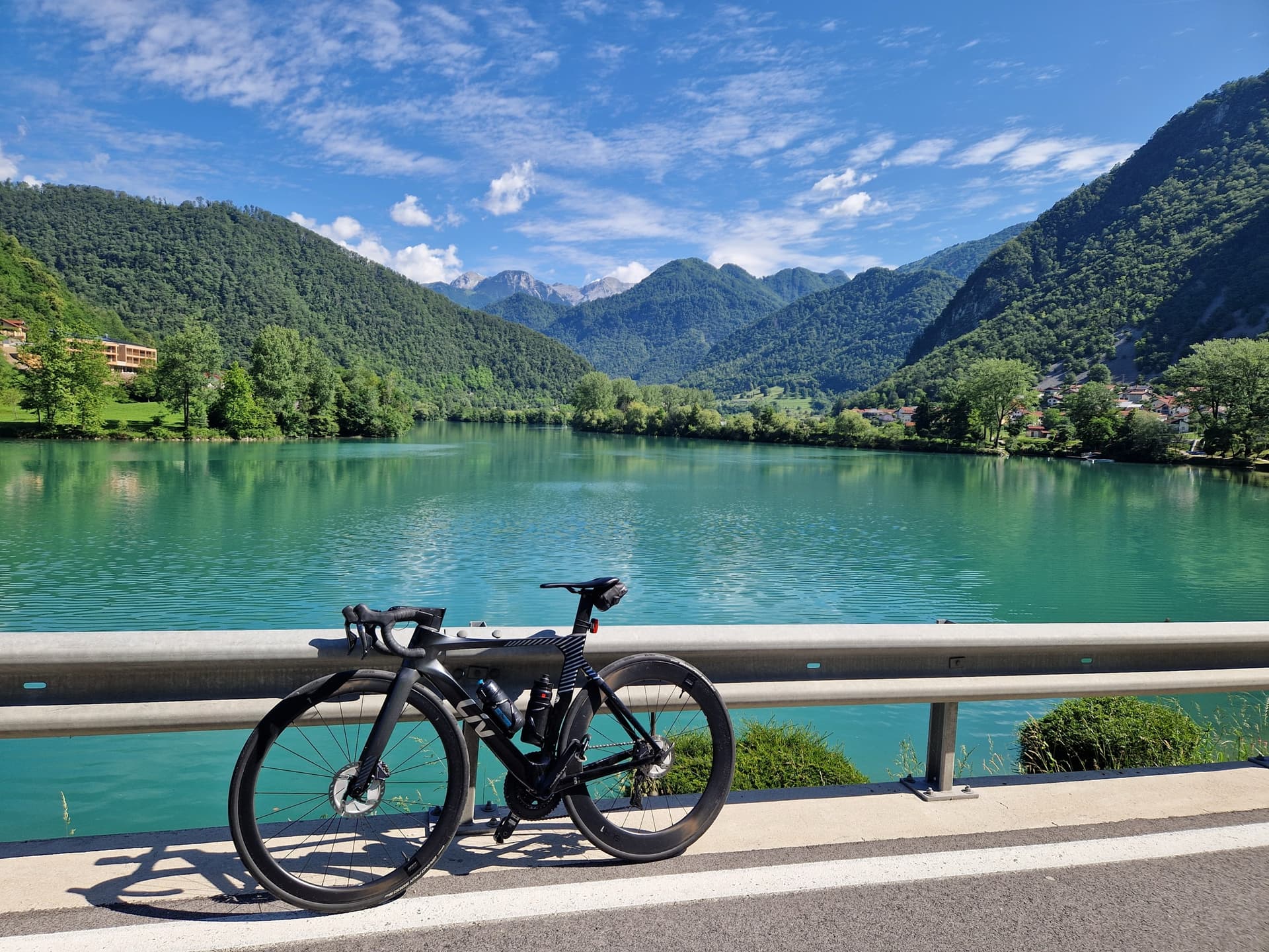 Road bike parked by a green lake with mountains and blue sky