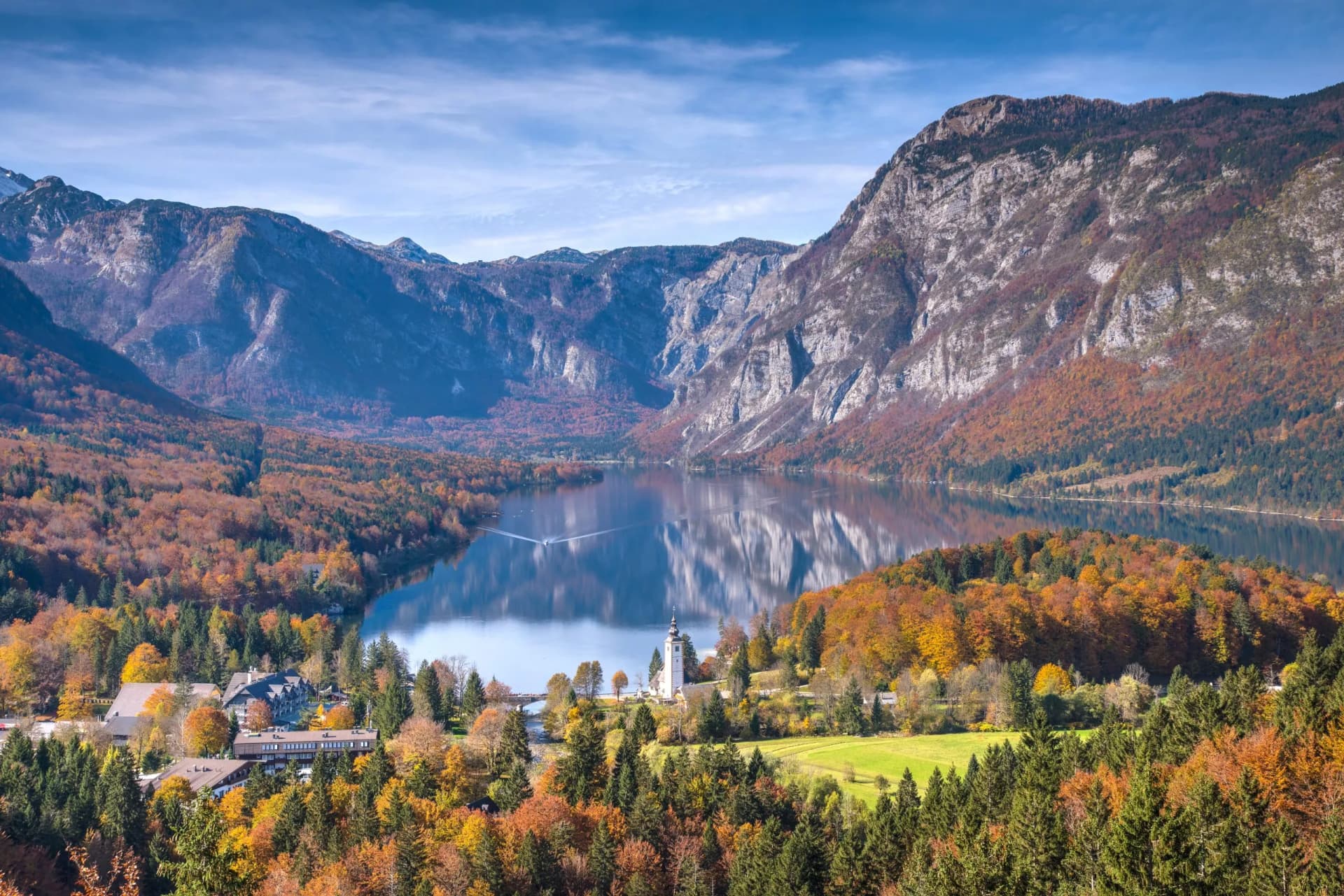 Lake Bohinj with autumn foliage, mountains, and a church by the reflective water.