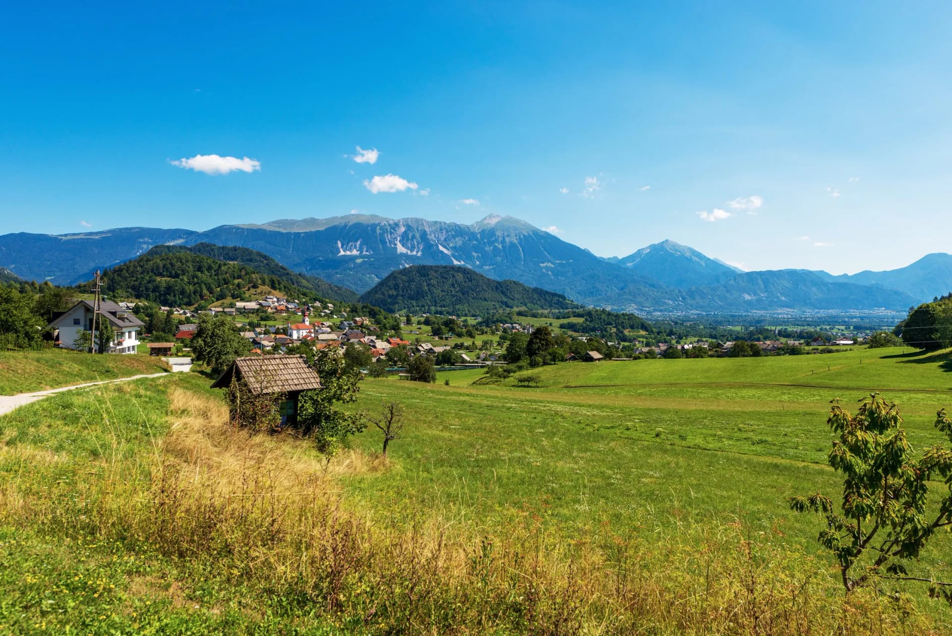Rural village nestled in green hills with large, rugged Alps in Upper Carniola background.