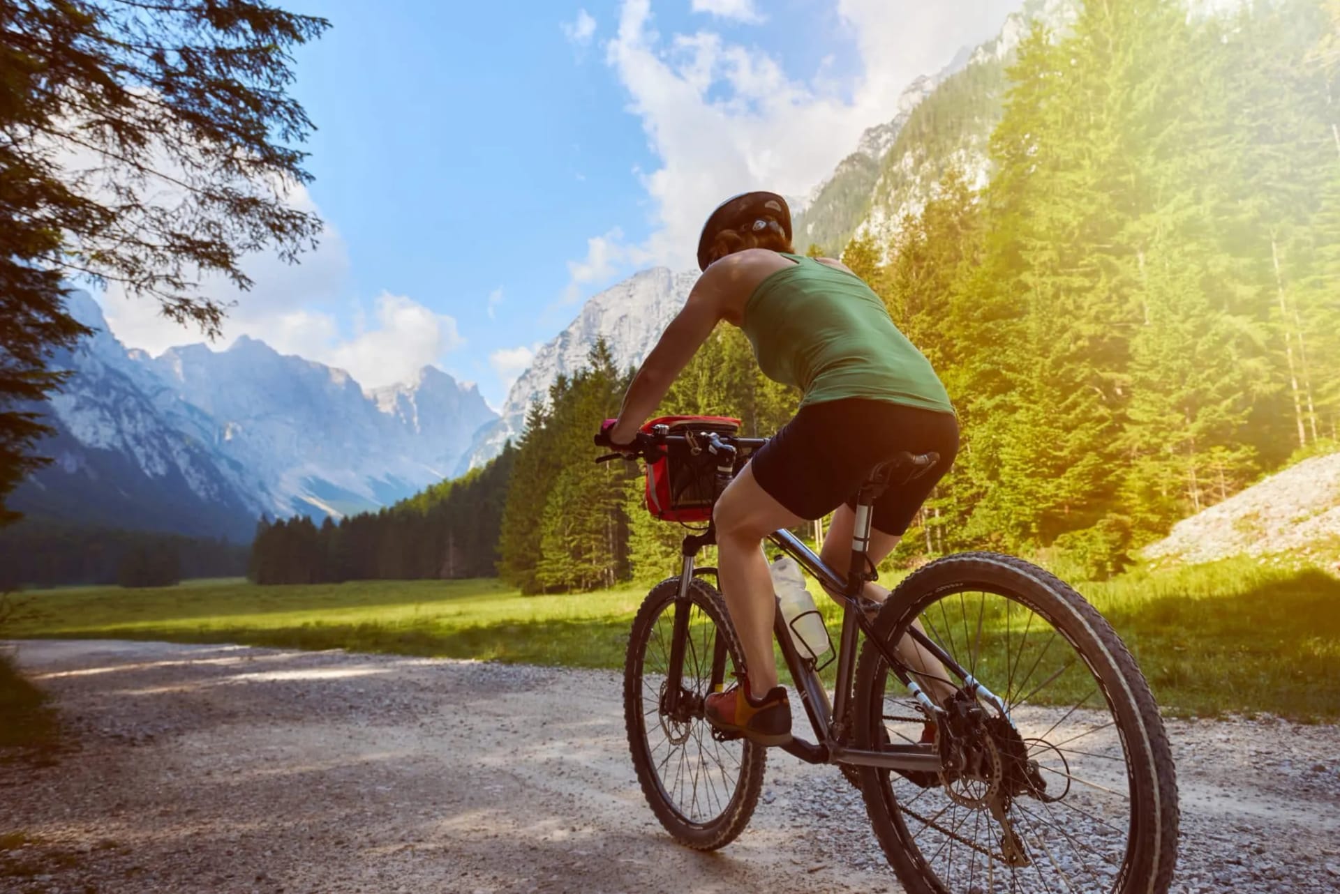Mountain biking on a gravel path through an alpine valley with tall peaks and pine forests.