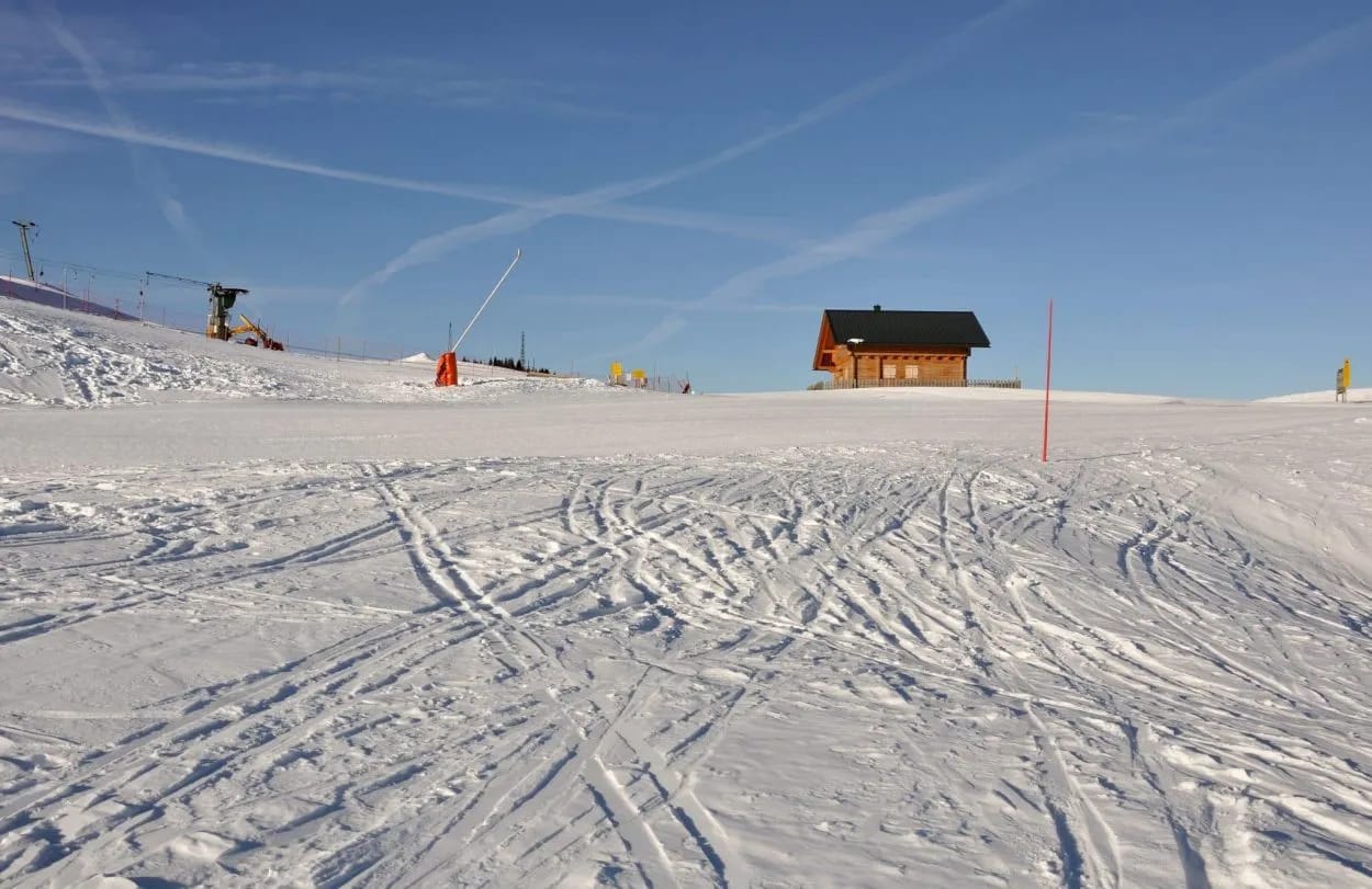 Ski slope with many tracks leading toward a wooden cabin under a clear blue sky at Dreilandereck-Arnoldstein.
