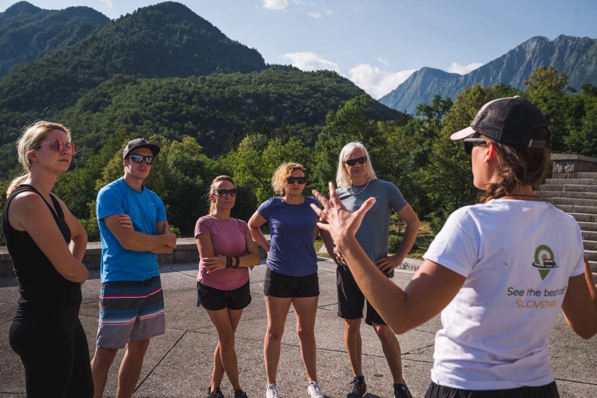 Tour group listening to guide with lush green mountains in Slovenia background
