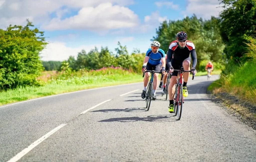 Group of road cyclists riding on an asphalt road through green countryside under a blue sky.