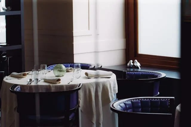 Set dining table with white linen, glassware, and purple leather chairs inside a restaurant.