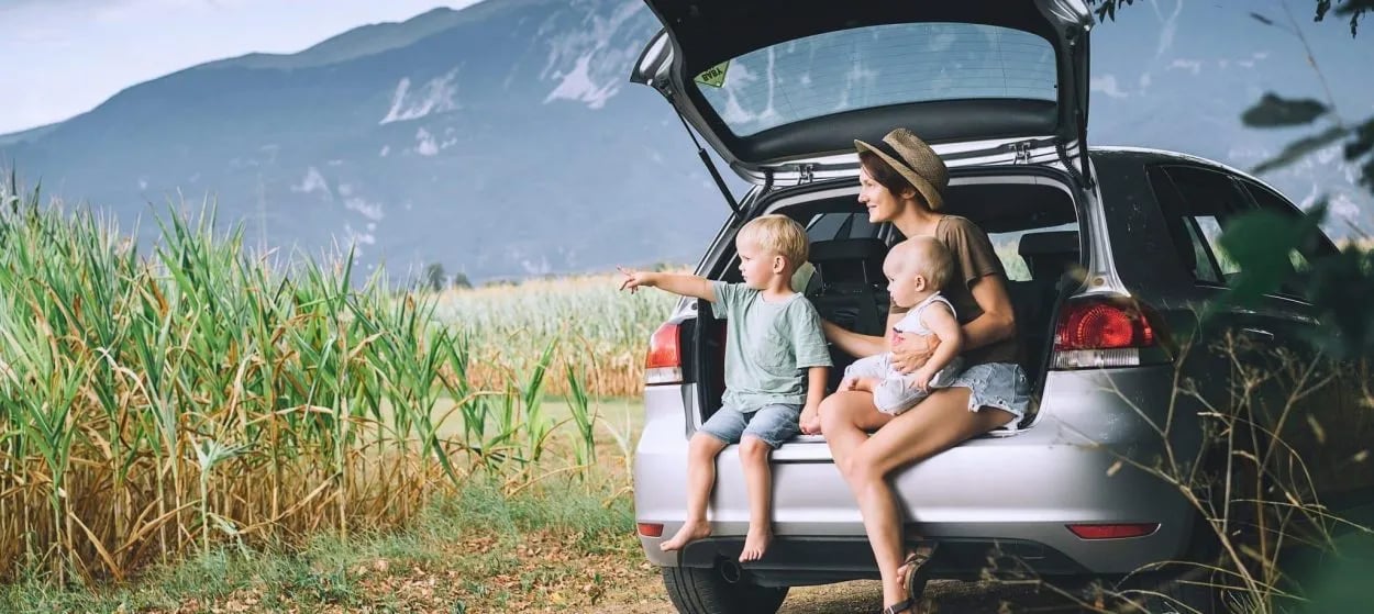 Family resting by car trunk in field with mountains in background near Bohinj