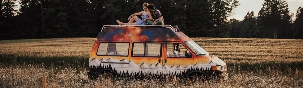 Camper van with sunset mural parked in a field with couple on roof, Balkan travel.