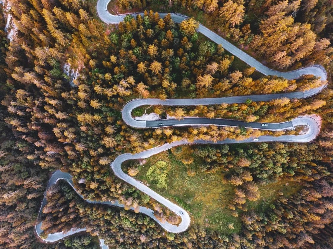 Aerial view of winding mountain road with switchbacks through autumn forest foliage.