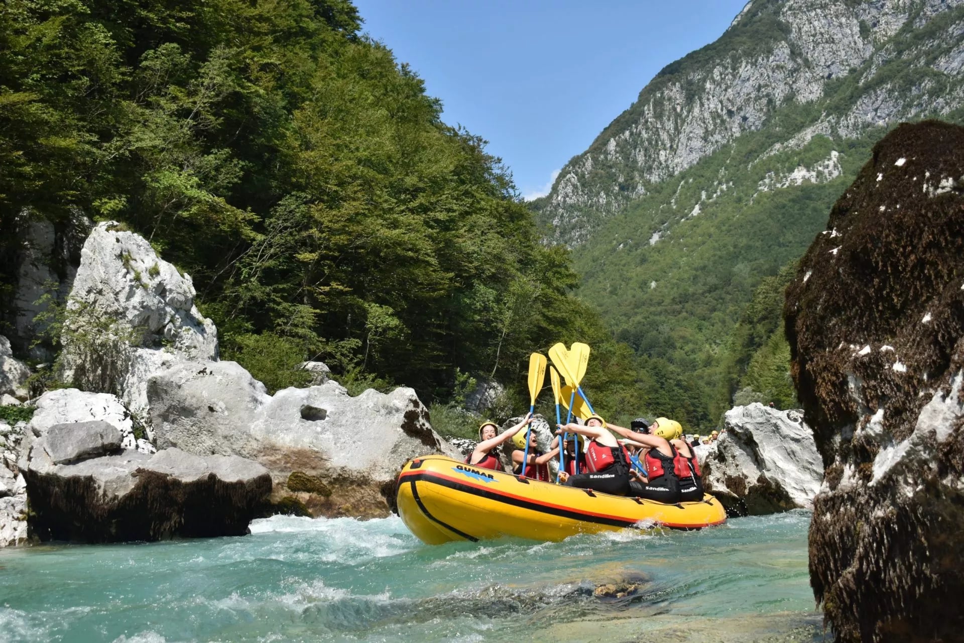 White-water rafting on turquoise river rapids surrounded by steep, forested mountains.