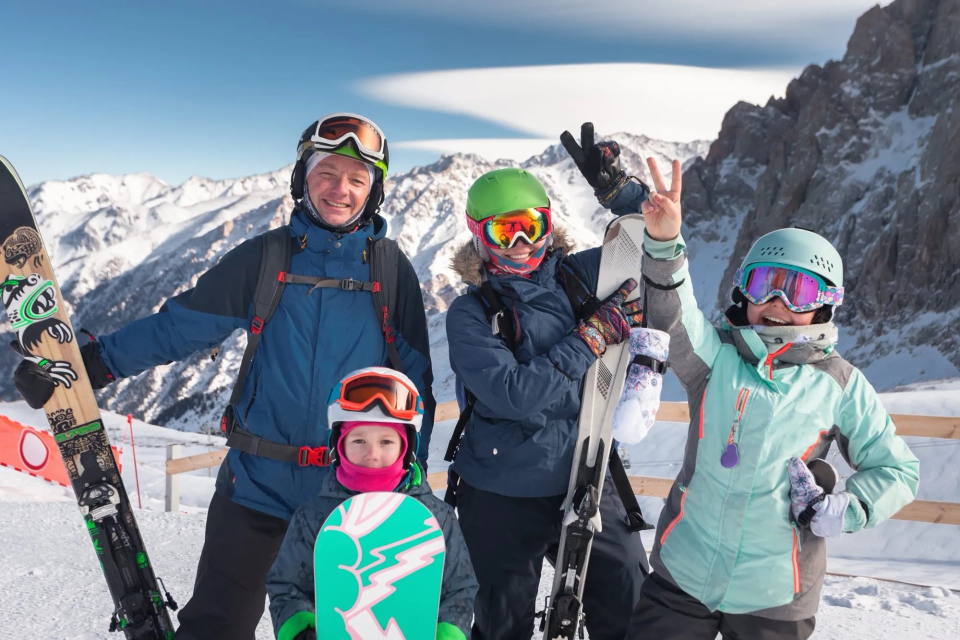 Family posing with snowboards and skis on snowy mountain slope under blue sky