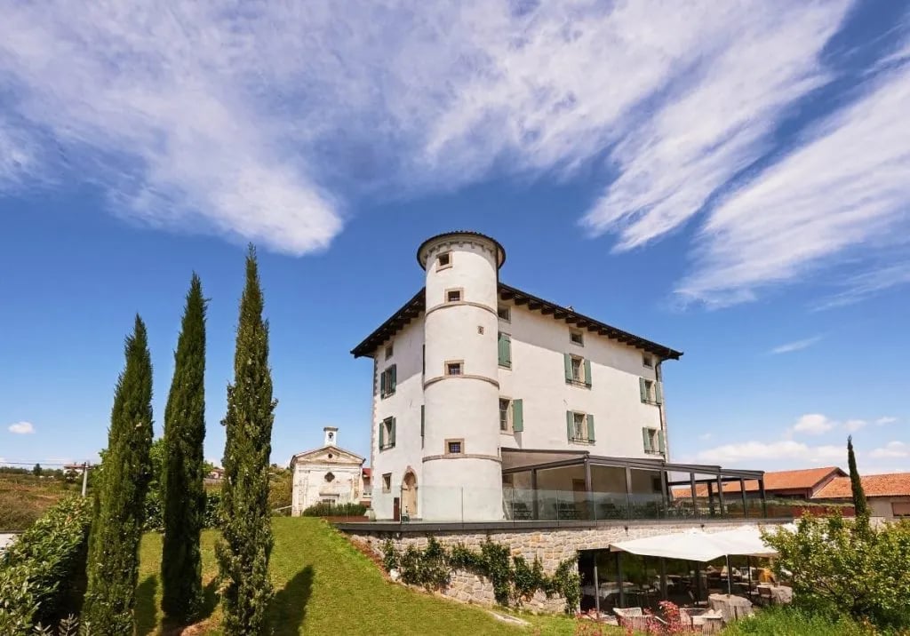 White historic building with round tower, cypress trees, and blue sky with wispy clouds.